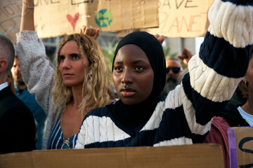 Serious Muslim woman holding a banner in a protest by a group of people at a demonstration on...