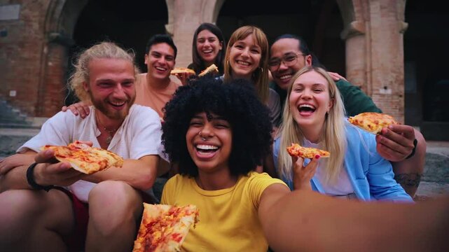 Funny selfie of a group of young people eating pizza in the touristic city. Italian friends having food outdoors, laughing in a casual street setting. Vibrant urban background and cheerful mood