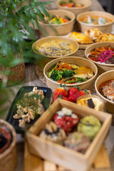 Colorful display of multiple take-away bowls with healthy dishes, desserts, including soups, vegetables, meat, empanadas, strawberries, and cookies. Trendy food delivery concept, recyclable packaging.