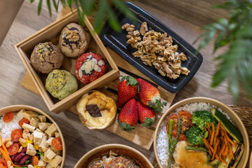 Top view of a colorful food arrangement, assorted desserts. Artisan cookies in a wooden box, strawberries, cheesecake, a black walnuts tray. Carefully styled on a wooden surface with vibrant tones.