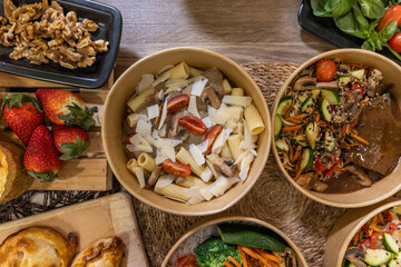 Top view of rigatoni pasta with creamy mushroom sauce, cherry tomatoes, and grated cheese in a paper bowl. Takeaway restaurant concept, eco-friendly packaging.