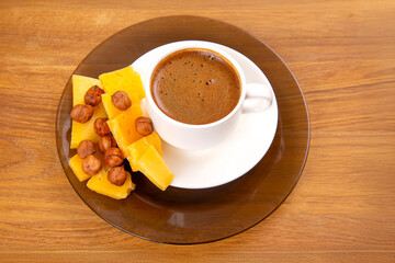 An overhead shot of a frothy espresso in a white cup, resting on a saucer, accompanied by vibrant yellow cheese slices on a cozy wooden table surface