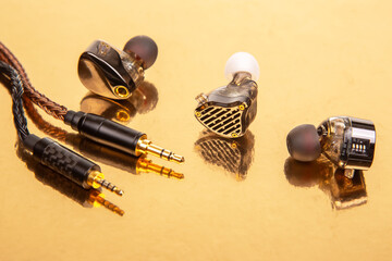 Three earbuds with braided cables and 3.5mm plugs on a gold surface, great for showcasing audio accessories and tech equipment.