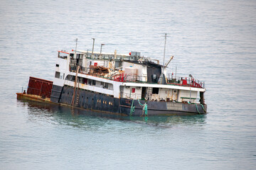 Rusty old cargo ship floating on calm sea waters, showing signs of wear with faded paint and...