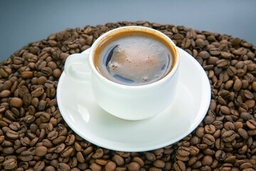 Top view of a steaming espresso in a white cup, its golden crema contrasting with the surrounding roasted coffee beans, all resting on a simple white saucer.