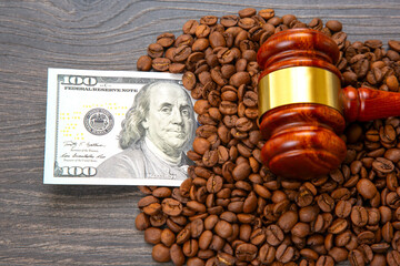 A wooden gavel on coffee beans with a $100 bill nearby on a dark wood backdrop, depicting the...