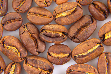 Up-close perspective of roasted coffee beans with visible splits and a smooth, dark brown finish on a white background. Perfect for coffee shop marketing.