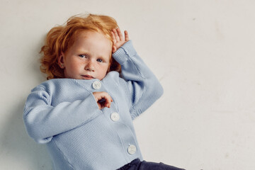 Little red haired girl daydreaming on the floor in front of a white wall, dreamy childhood beauty...