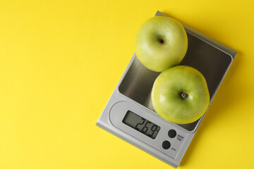 Electronic kitchen scale with apples on yellow background, top view. Space for text