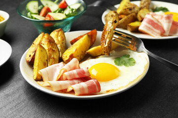Tasty brunch. Fried egg, potato, bacon and fork on dark textured table, closeup