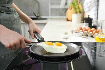 Woman taking fried eggs from frying pan in kitchen, closeup