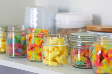 Tasty gummy candies in jars on shelf, closeup