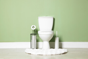 Ceramic toilet bowl, brush and paper near green wall indoors
