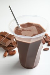 Tasty chocolate milk, bars and cocoa beans on white wooden table, closeup