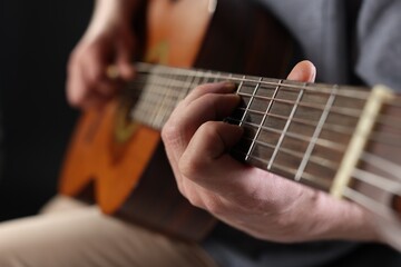Obraz premium Man playing guitar on black background, focus on hand