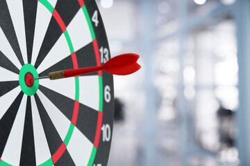 Targeting and business success. Dart sticking in center of dartboard in office, closeup
