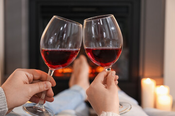 Couple with glasses of wine near fireplace at home, closeup