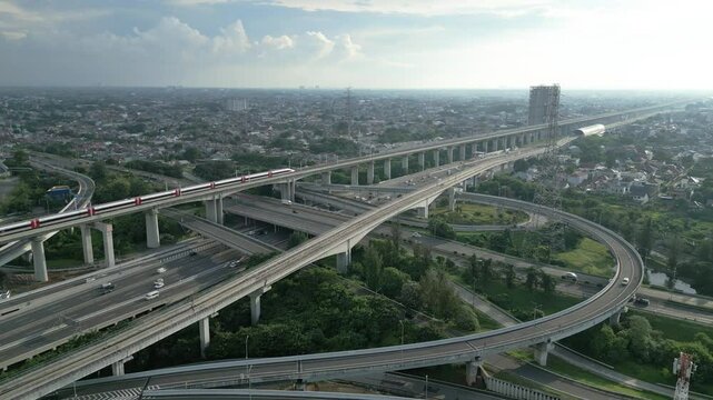 Aerial view of Jakarta - Bandung high-speed train on an elevated track above a busy toll road at sunset in Indonesia.