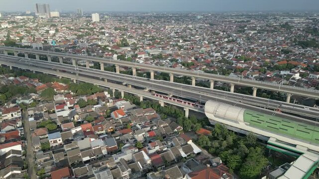 Aerial view of LRT commuter train passing through elevated tracks above highway and urban neighborhood in Jakarta, Indonesia.
