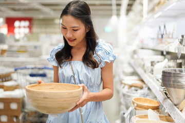 asian woman looking at wooden bowl in homeware store aisle