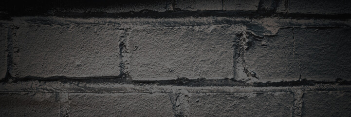 Old brick wall. The texture of weathered grungy brickwork. Panorama of a wall with a rough masonry surface. Dark wide panoramic background for design. Shaded vintage texture with dark vignette.
