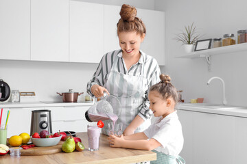 Mother and little daughter pouring smoothie into glasses in kitchen