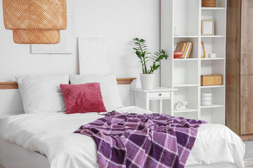 Interior of modern bedroom with shelving unit, houseplant and purple blanket on bed