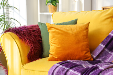 Stylish yellow sofa with pillows and purple plaid in living room, closeup