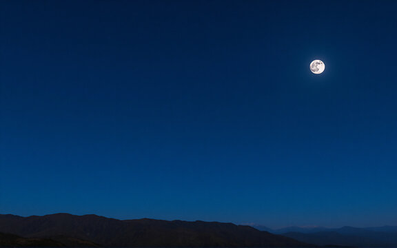 A bright full moon illuminates the dark blue night sky over a silhouette of distant mountains. A peaceful and serene outdoor scene.