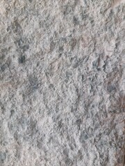 Close-up image of a rough textured stone surface with a mix of gray, white, and light brown tones,...