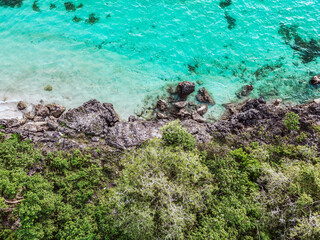 Clear turquoise sea surrounding rocky cliffs and vibrant green tropical forest on island coast