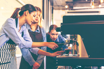 Female barista making coffee in coffee shop counter. Takeaway food. Professional coffee making. Small business.Asian woman entrepreneur making coffee from machine while standing by coworker at cafe. 