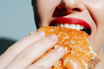 Young woman with red lipstick joyfully biting into a delicious hamburger, showcasing a vibrant and appetizing food moment.