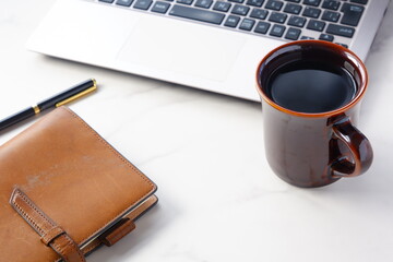 淹れたての美味しいコーヒーを飲みながら、ノートパソコンとシステム手帳でデスクワークをしているイメージ
