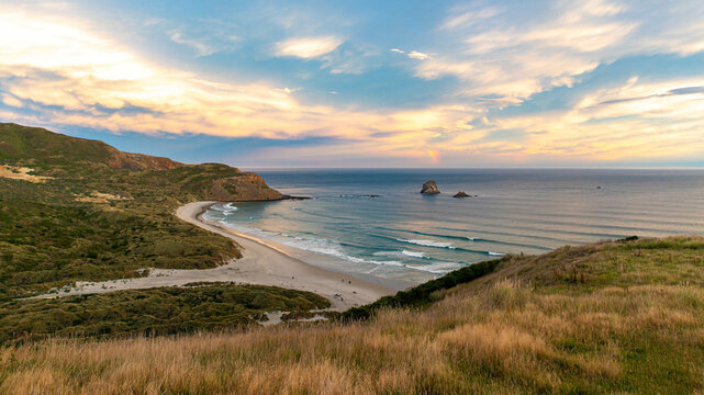 sunset over stunning Sandfly Bay with powerful waves. Amazing beach with striking rock formations in the ocean, Otago Peninsula, Dunedin, South Island, New Zealand