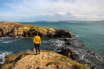 Relaxed girl standing and admiring views of the Pacific Ocean and rocky shoreline by Katiki Point...