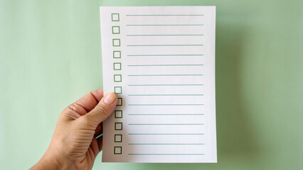hand holding blank checklist paper with green boxes and lines on pastel green.