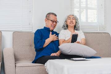 Elderly couple sitting on sofa, smiling and enjoying moment while looking at smartphone together.