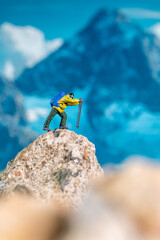 Miniature Climber Reaches Summit Against Majestic Mountain Backdrop
