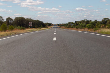 A straight, open highway stretching into the Australian outback under a sky filled with scattered clouds