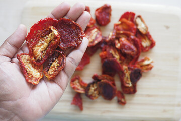 Dried tomatoes being held in hand over a wooden chopping board
