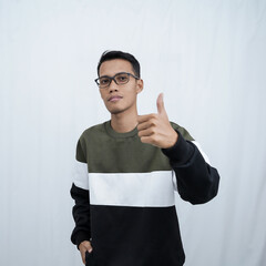 An Asian young man with glasses wearing a sweater smiling expression while giving a thumbs up sign. Isolated on white background.