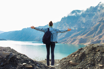 Young woman with backpack standing on top of mountain and looking at the blue lake
