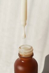 A drop of cosmetic product drips from a pipette into a small brown jar. Facial skin serum. A...