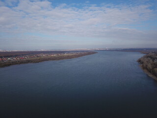 Serene aerial view of vast river under partly cloudy sky with distant cityscape