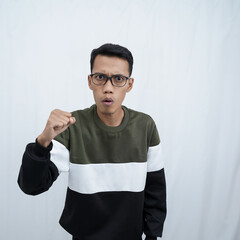 A young Asian man with glasses wearing a sweater with a happy, excited, triumphant expression while raising and clenching his fist. Isolated on white background.