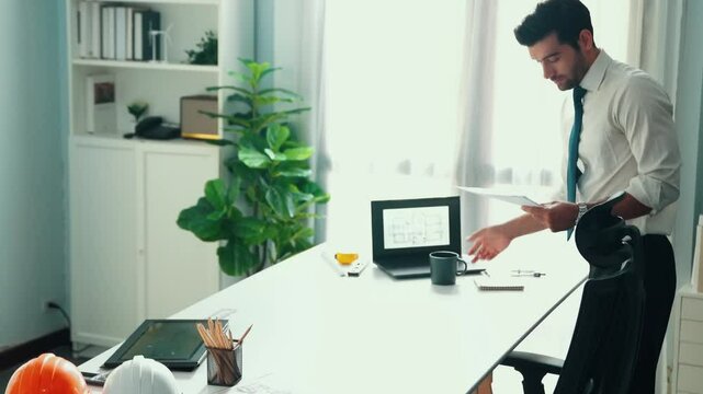 Architect engineer using laptop planning house design at office while sitting at meeting table with blueprint and equipment scatter around.Skilled civil engineer working at blueprint. Alimentation.
