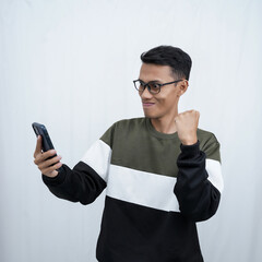 A young Asian man with glasses wearing a sweater with a surprised happy expression getting a surprise while looking at a smartphone. Isolated on a white background.