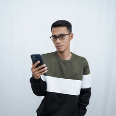 An Asian young man with glasses wearing a sweater holding a smartphone. Isolated on white background.