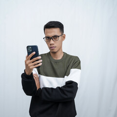 An Asian young man with glasses wearing a sweater holding a smartphone. Isolated on white background.